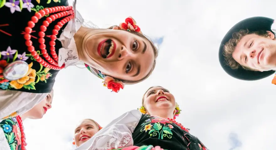 Uśmiechnięci młodzi ludzie w barwnych strojach ludowych, żywa ludowa twórczość artystyczna.