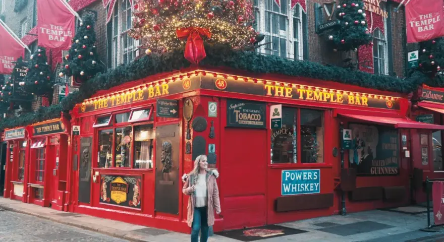 Una mujer pasea por la calle empedrada frente al icónico pub The Temple Bar en Dublín, decorado para Navidad. ¡Una excelente idea de qué hacer en Dublín!