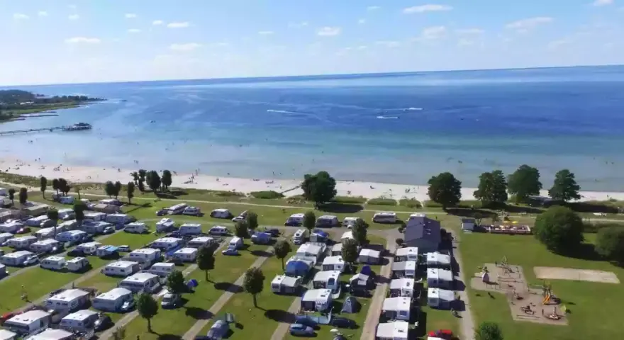 En stor campingplats vid havet nära Kalmar. Husvagnar och husbilar står uppradade på gräsmattor, med en strand och brygga i bakgrunden.
