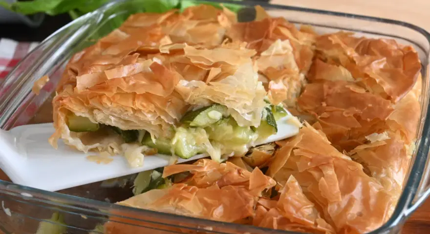 Una fetta di torta salata con zucchine, con croccante pasta sfoglia dorata e ripieno filante.