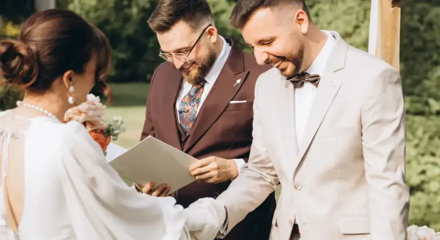 Uroczystość ślubna: panna młoda w białej sukni, pan młody w jasnym garniturze i urzędnik. To piękny ślub humanistyczny, a nie tylko cywilny.