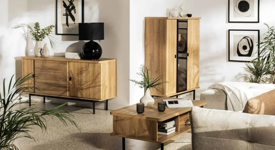 Drewniane meble i subtelne dodatki tworzą przytulną atmosferę w stylu hygge. Wazon z gałązkami i czarna lampa dodają elegancji.