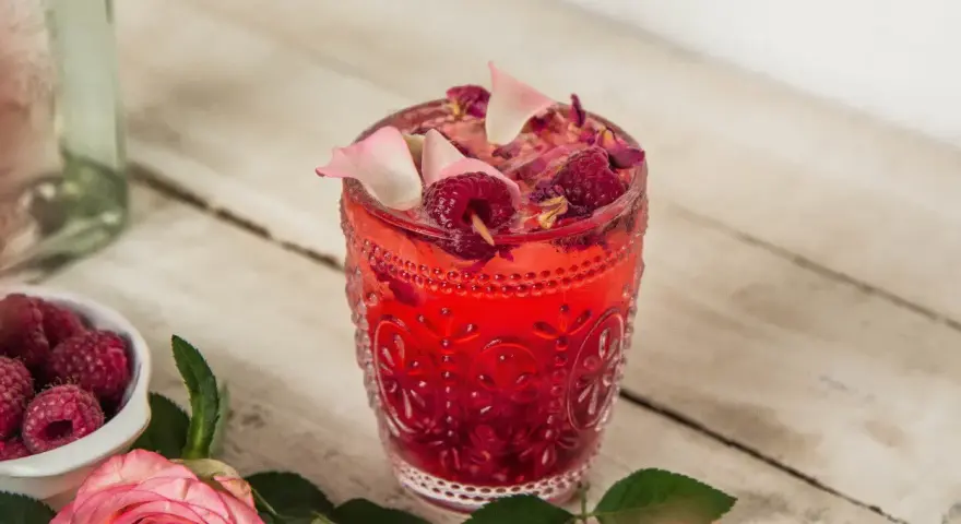 Orzeźwiający drink z malinami, ozdobiony płatkami róż i świeżymi malinami. Idealny na letnie popołudnie.