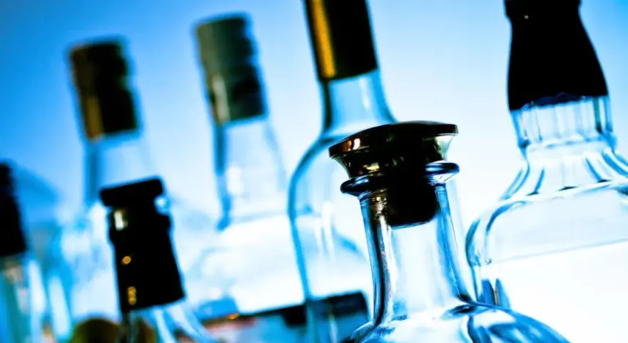 Kilka szklanych butelek alkoholu na niebieskim tle.