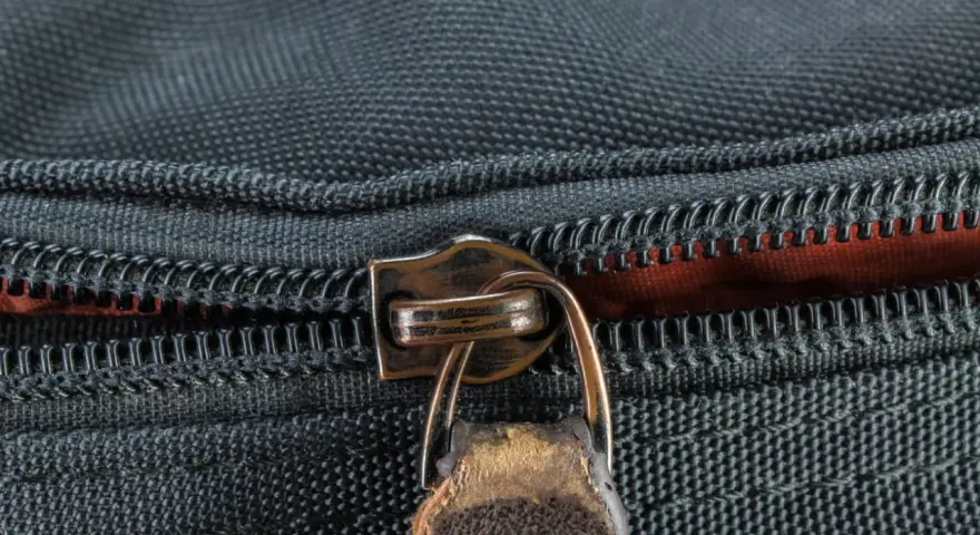 Nahaufnahme eines Reißverschlusses an einer schwarzen Tasche. Der Schieber ist aus Metall und leicht abgenutzt, was auf die Notwendigkeit hinweist, den Reißverschluss zu reparieren.