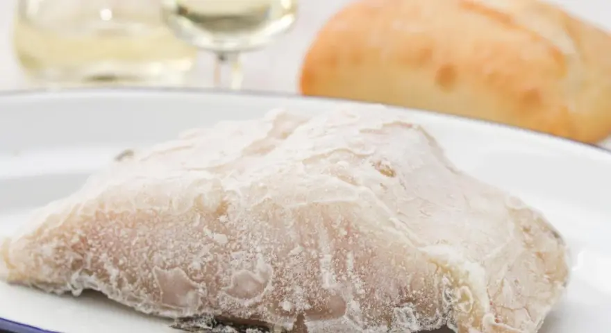 Un trozo de pescado en blanco, escarchado, listo para cocinar. Acompañado de pan y vino blanco.