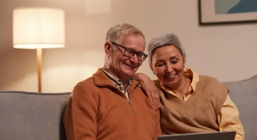 Uśmiechnięta para seniorów przegląda coś na laptopie. Zastanawiają się, czy zwolnienia lekarskie mają wpływ na wysokość emerytury.