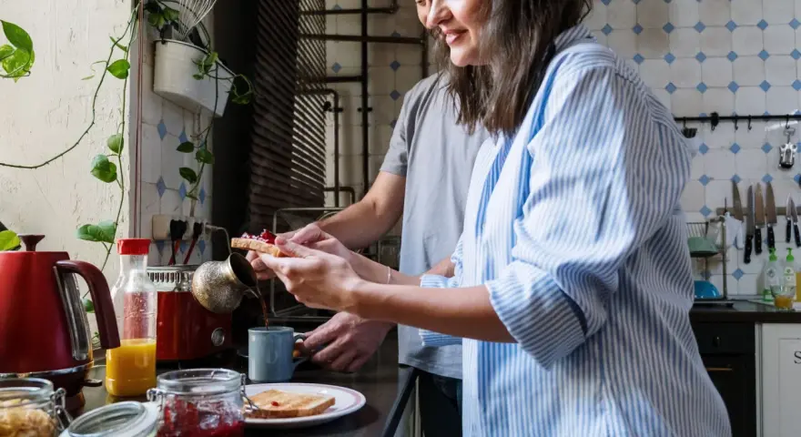 Pareja preparando el desayuno, tostadas con mermelada y café. Un momento de "bonjour" en francés para empezar el día.