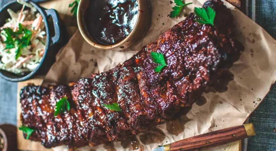 Saftiga spareribs i ugn, glaserade och serverade med en skål coleslaw och BBQ-sås. Perfekt för en festmåltid!