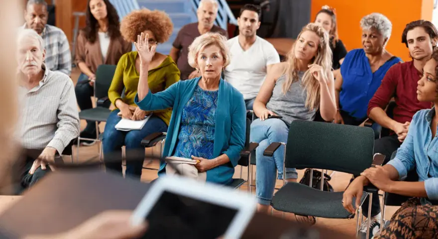 Una mujer levanta la mano en una reunión, mostrando que cualquiera puede ser presidente de una comunidad.