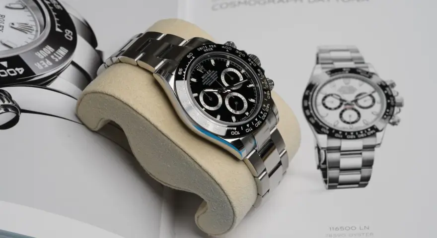 Luxuriöse Rolex Daytona Uhr auf einem Kissen vor einem Buch mit Uhrenabbildungen.