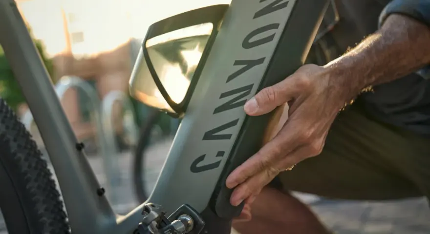 En hand justerar en elcykel. Solen skiner genom ett fönster på cykelns ram.