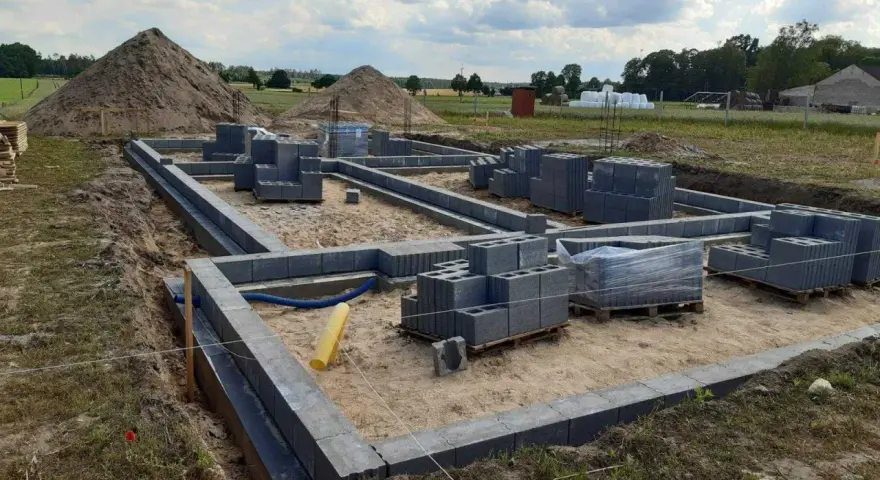 Budowa fundamentów z bloczków betonowych. Zastanawiasz się, ile kosztuje wylanie fundamentu? Na placu budowy widać materiały i postęp prac.