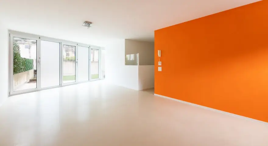 Jasne, nowoczesne wnętrze z pomarańczową ścianą i podłogą z **mikrobetonu**. Duże okna wpuszczają dużo światła.