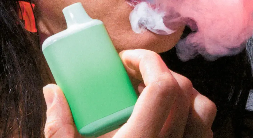 Persona vapeando un dispositivo verde, exhalando vapor. Una imagen que ilustra la diferencia entre vapear y fumar.