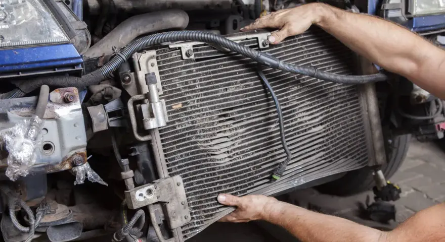 Mechanic removing a car's AC condenser, which blows hot air, for repair.