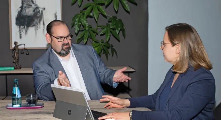 Ein Anwalt für Krankenversicherungsrecht erklärt einer Mandantin am Tisch komplexe Sachverhalte.