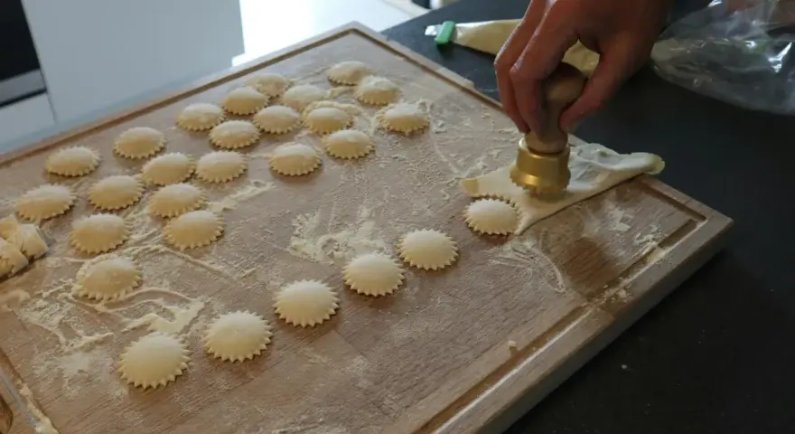 Ręcznie robione ciasto na ravioli, wycinane okrągłym wykrawaczem. Widać wiele gotowych krążków na desce.