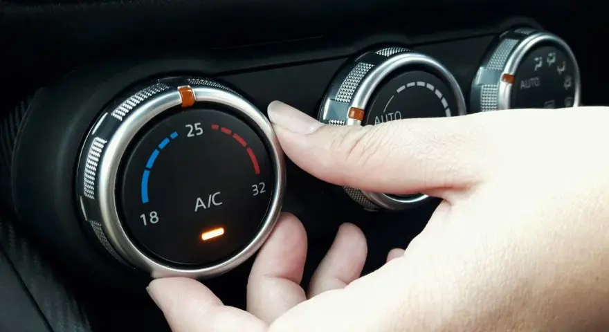 Dłoń reguluje pokrętłem temperaturę klimatyzacji w samochodzie, ustawiając ją na 25 stopni.