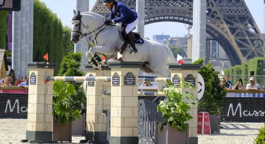 Un cavalier et son cheval blanc, Rahotep de Toscane, franchissent un obstacle à Paris, avec la Tour Eiffel en arrière-plan.