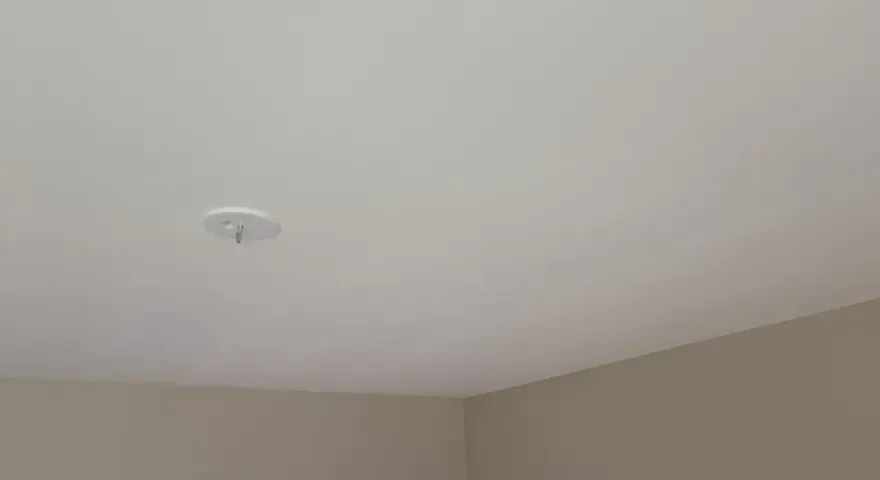 Ett vitt tak med en krok för en lampa. Väggarna är ljusbruna. Snart dags att måla taket för en fräschare känsla.