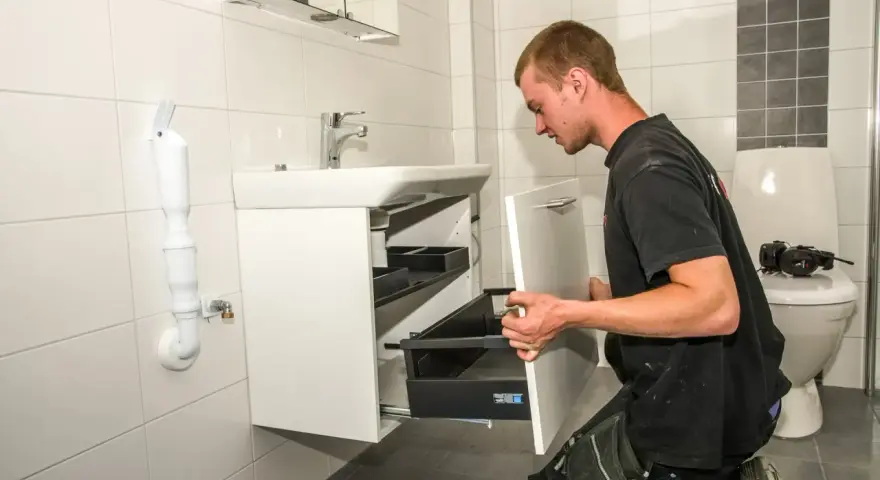 En rörmokare utför vvs arbeten i ett badrum, monterar ett nytt handfat och skåp.