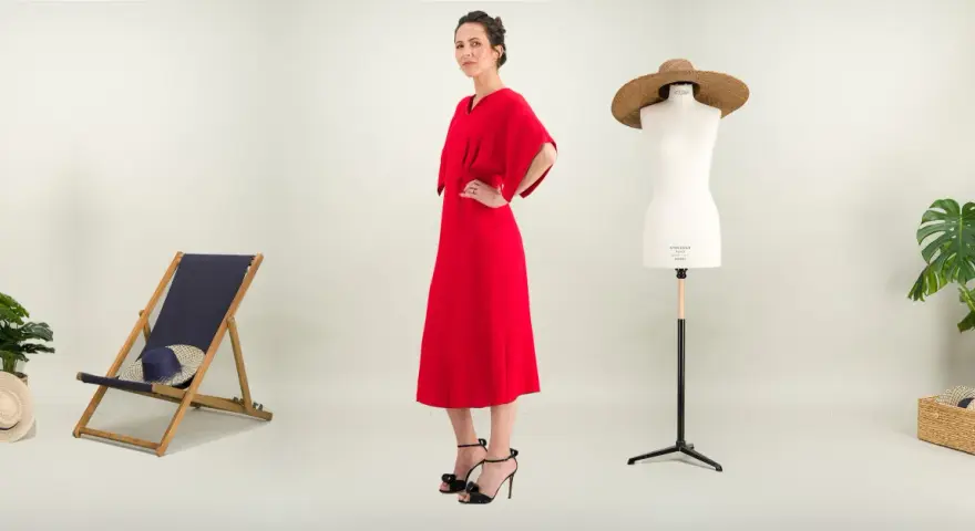 Une femme pose dans une robe rouge éclatante. À ses côtés, une chaise longue, un mannequin de couture et des plantes. Une robe casual, c'est quoi ?