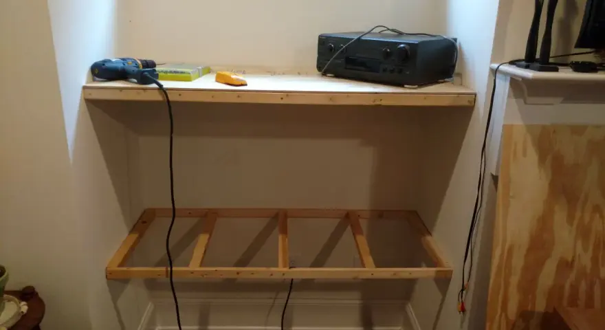 DIY project: a drill, screws, and audio receiver are on a shelf, with a wooden frame below, ready for how to hang shelves.