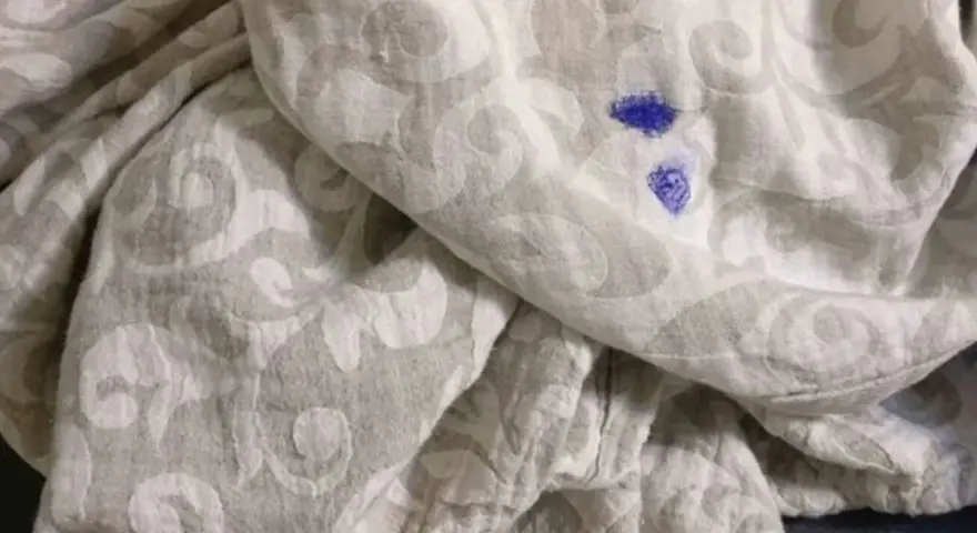 Niebieska plama po flamastrze na jasnej tkaninie z wzorem. Jak zmyć flamaster z ubrania?