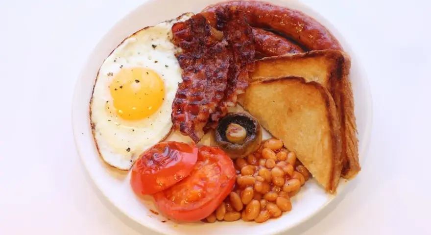 Un piatto tipico inglese con uovo fritto, bacon croccante, salsiccia, fagioli stufati, pomodori grigliati, fungo e toast.
