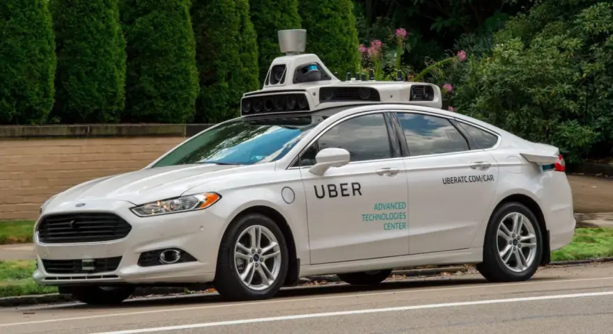 Ein weißes Uber auto mit Sensoren auf dem Dach fährt auf einer Straße.