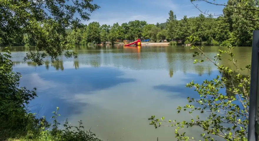Idyllischer sulzfeld badesee mit Spielplatz und Rutsche, umgeben von grünen Bäumen.