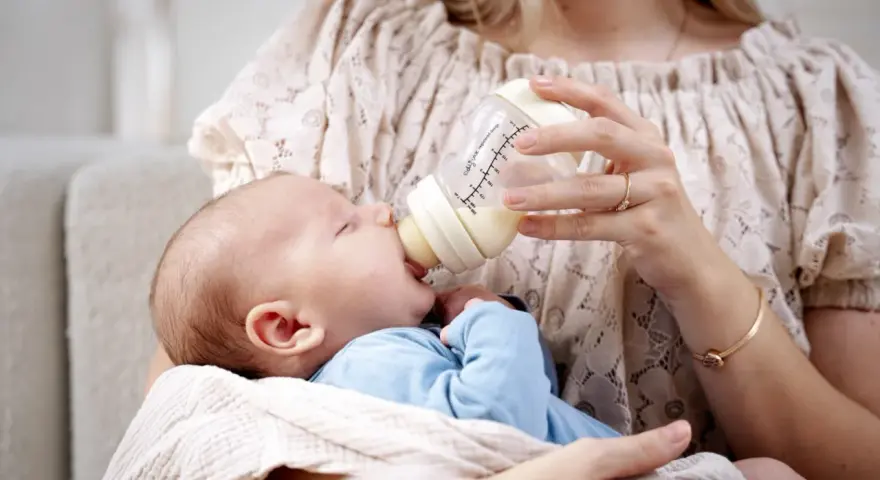 Mama karmi maluszka z butelki, która może być najlepszą butelką antykolkową dla noworodka.