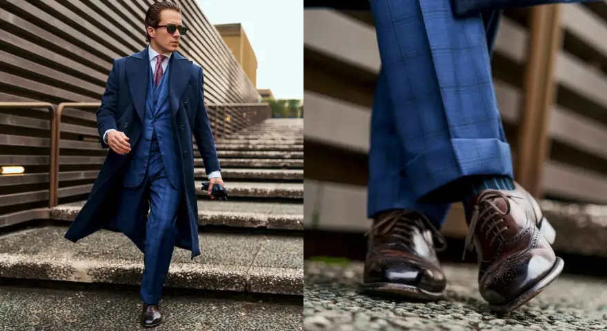 Un giovane uomo con un completo blu a quadri, cappotto scuro e occhiali da sole, cammina con passo sicuro. Un vero old money boy.