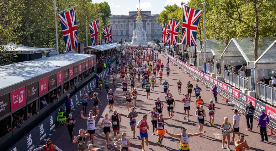 Tysiące biegaczy na trasie maratonu londyn, z flagami Wielkiej Brytanii i Pałacem Buckingham w tle.