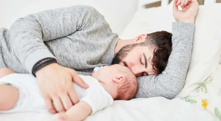 Padre e neonato nel lettone in sicurezza, un momento di dolce riposo e amore.