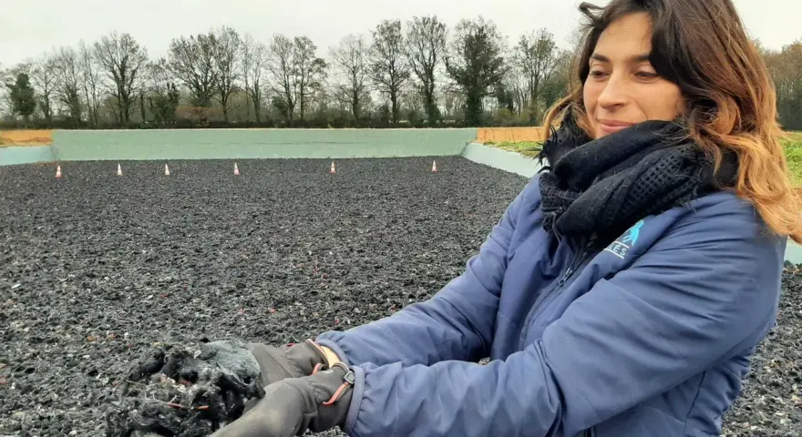 Une femme tient dans ses mains un échantillon de fibre, un avis carrière en fibre. L'arrière-plan montre une carrière équestre.
