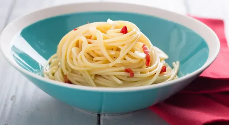 Spaghetti aglio e olio, czyli spaghetti bez mięsa z czosnkiem i papryczką chili, podane w turkusowej misce.