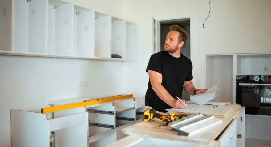 Mężczyzna planuje, jak zabudować przestrzeń nad szafkami kuchennymi, analizując projekt.