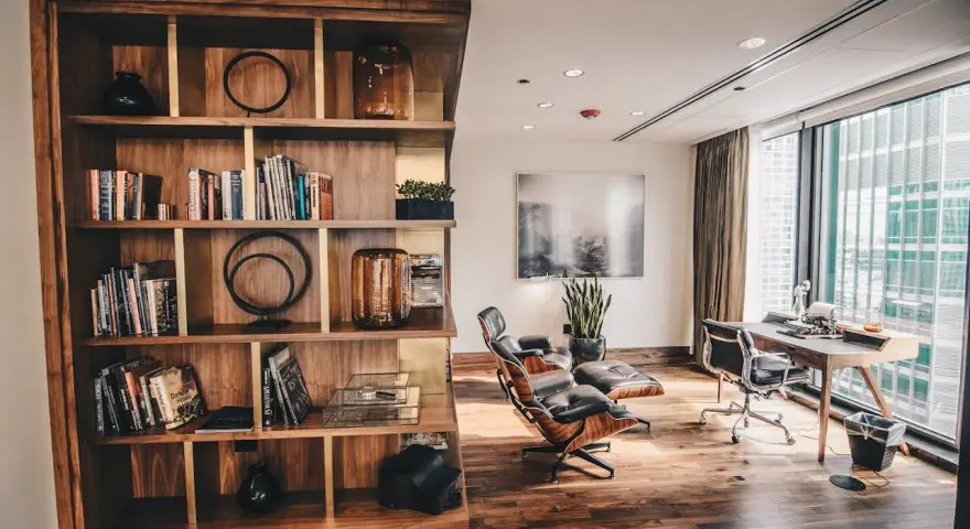 Drewniana biblioteczka z książkami i dekoracjami, obok skórzane fotele i biurko z maszyną do pisania. Styl **modern rustic**.