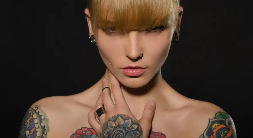 Kobieta z tatuażami na klatce piersiowej i ramionach, kolczykami w uszach i nosie. Czy tatuaże są szkodliwe?