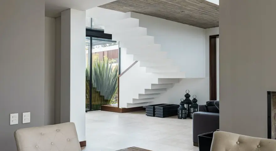 Moderna escalera blanca con un diseño flotante. El **rellano escalera decoracion descansillo escalera** se realza con linternas negras y maceteros.