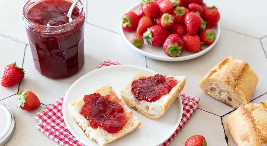 Un pot de confiture de fraise maison, des tartines de pain frais garnies de cette confiture, et des fraises fraîches. Un délice !