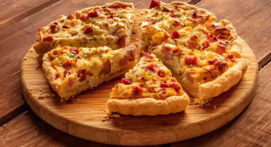 Fette di torta salata patate e salsiccia dorata e invitante, servite su un tagliere di legno.