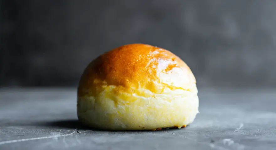Ein goldbraunes Brioche-Brötchen liegt auf einer dunklen Oberfläche.