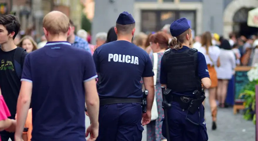 Policja w patrolu, kiedy policja szuka dłużnika. Dwóch funkcjonariuszy w mundurach idzie ulicą wśród tłumu ludzi.