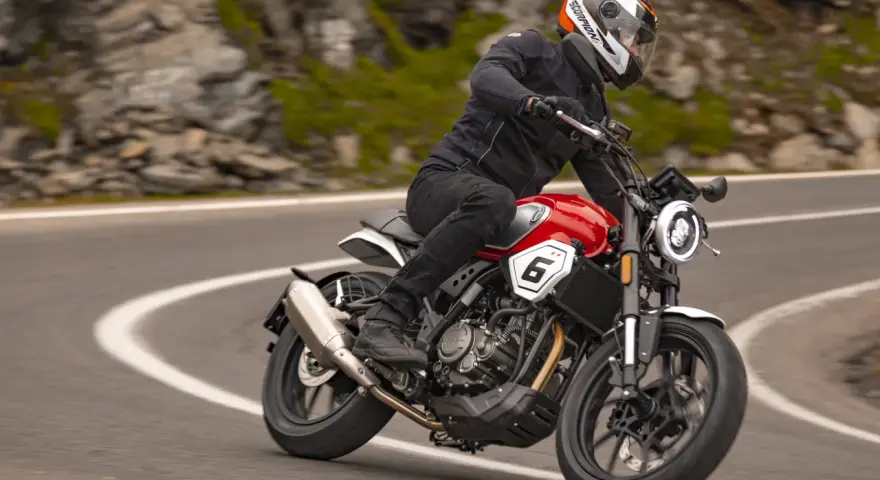 Motocyklista w kasku jedzie czerwonym motocyklem po krętej drodze. Idealny motocykl na początek przygody z jazdą.