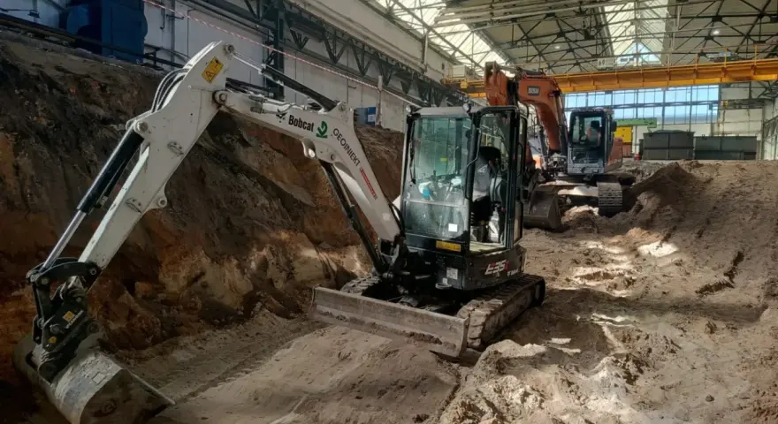 Koparki pracują w hali, przygotowując teren. Trwa wymiana gruntu, cena za m3 jest kluczowa dla budżetu.