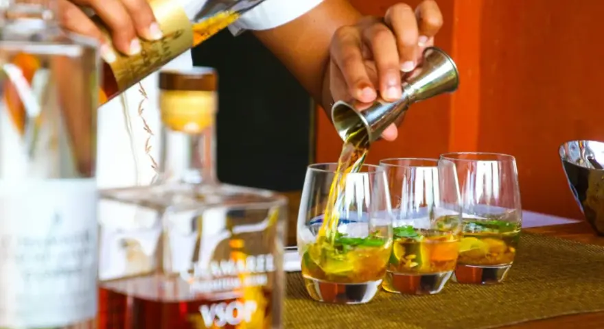 Ein Barkeeper gießt bernsteinfarbenen Rum in Gläser mit Eis und Minze. Die Frage "ab wann brennt Schnaps" wird hier durch das Servieren von edlem Rum beantwortet.