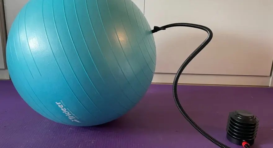 Niebieska piłka fitness podłączona do pompki na fioletowej macie.
